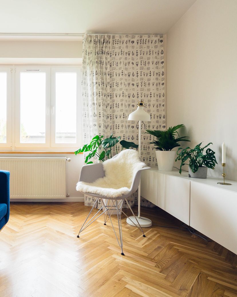 Jasny salon z niebieską sofą, lampą podłogową i białą szafką RTV na parkiecie w jodełkę